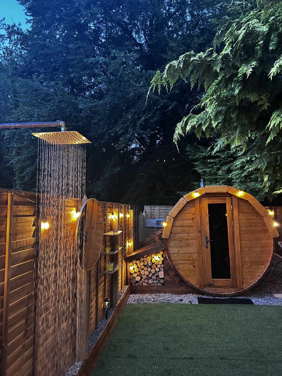 An Lasán barrel sauna and outdoor shower lit at dusk
